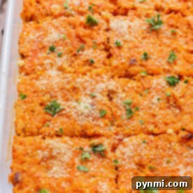 Baked sweet potato and carrot casserole in a dish, topped with breadcrumbs and fresh herbs, cut into square portions.