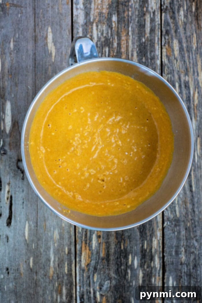 Spiced Maple Pumpkin Loaf 4 A bowl of maple pumpkin bread batter rests on a rustic wooden surface, ready for baking.