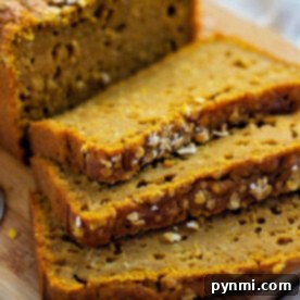Maple Pumpkin Bread, sliced and adorned with oats, is elegantly arranged on a wooden board.
