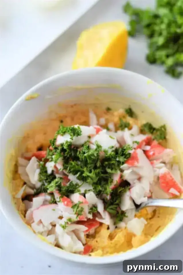 A bowl of mixed ingredients, including chopped imitation crab meat and a sprinkle of chopped parsley on top. 