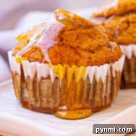 Perfect Gluten-Free Pumpkin Muffins 7 A gluten-free pumpkin muffin drizzled with honey sits on a white plate, with a blurred cloth in the background.