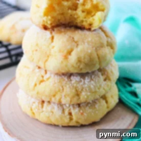 A stack of four delectable cake mix butter cookies, dusted with powdered sugar, sits on a wooden coaster. One has a playful bite taken from it, next to a vibrant green cloth.