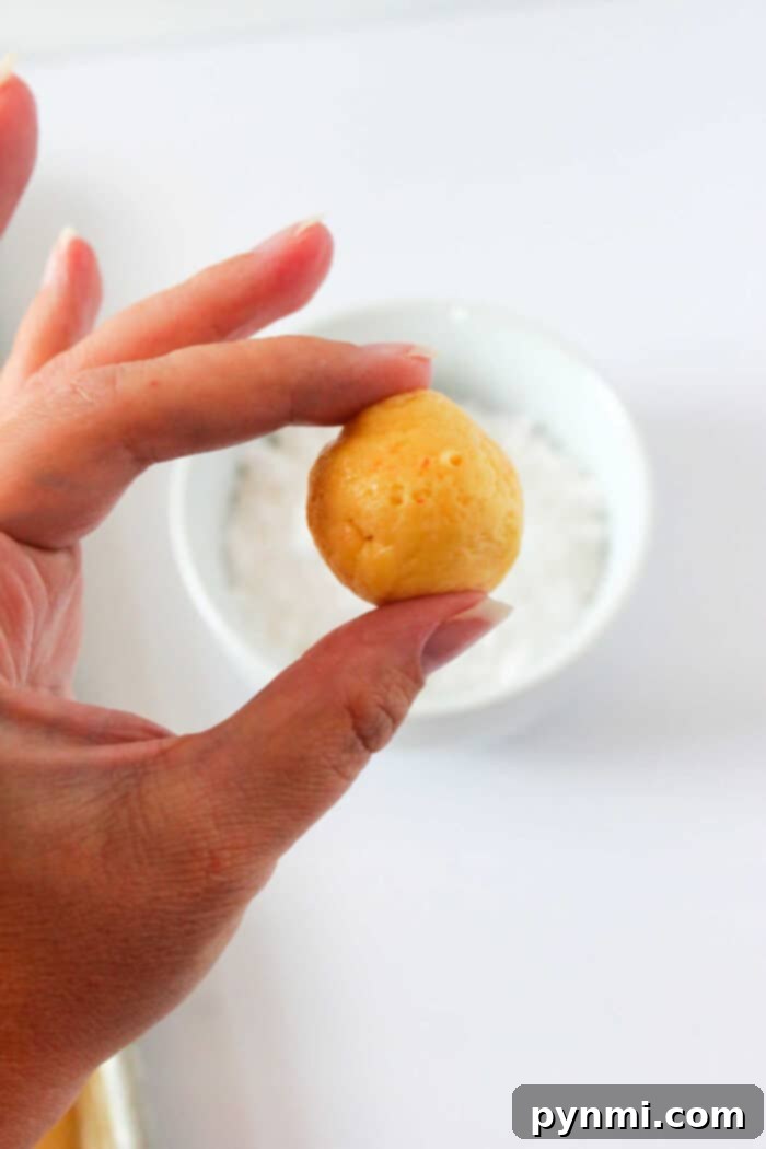 Rolling Cookie Dough in Powdered Sugar A hand delicately holds a small, round ball of cookie dough over a white bowl on a light background, evoking the satisfying allure of freshly baked cake mix butter cookies.
