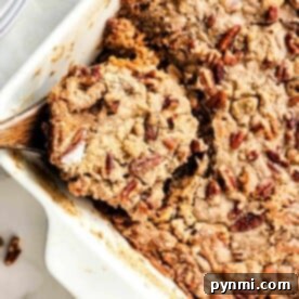 A close-up of a sweet potato dump cake-inspired pecan cobbler in a white baking dish, complete with a rustic wooden spoon.