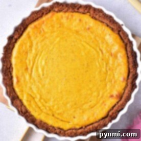Pumpkin Custard Pie in a white dish with a brown crust, next to a pink cloth and utensils.