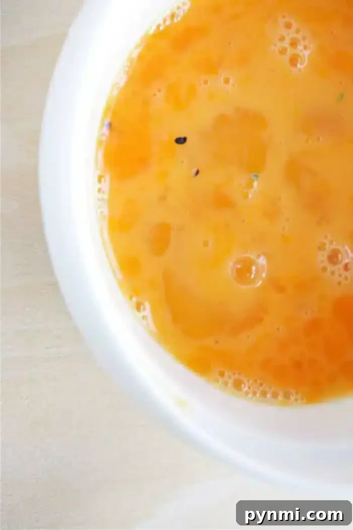 A close-up view of a bowl filled with a smooth, orange liquid, indicative of a perfectly prepared egg wash. Small bubbles suggest a well-whisked mixture, ready for application.