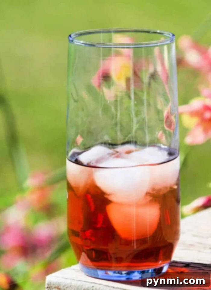 Brewing Sun Tea Perfection 2 A refreshing glass of sun tea with ice, fruit slices, and a tea pitcher in the background, set outdoors on a sunny day.
