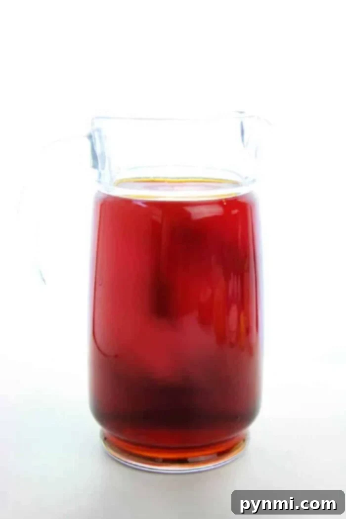 Brewing Sun Tea Perfection 5 A tall glass of cold brew iced tea with ice and lime slices, sitting on a wooden surface with a pitcher in the background.