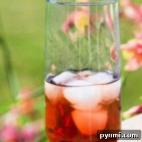 A tall glass of sun tea, made from a cherished recipe, with ice cubes clinking, sits on a wooden surface outdoors as vibrant flowers softly blur in the background.