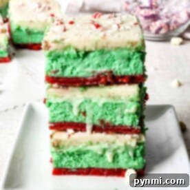 A delightful dessert lasagna of green and red layered cheesecake bars sits atop a sugar cookie crust, crowned with white frosting and sprinkled with crushed peppermint.