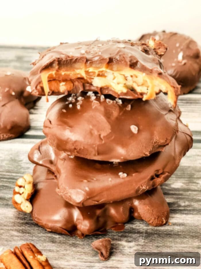 Decadent Pecan Caramel Bites 2 A stack of gourmet chocolate-covered caramel and pecan turtles, with sea salt flakes visible. The top candy shows a bite, revealing soft caramel and whole pecans. They rest on an inviting wooden surface.