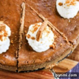 Gingerbread cheesecake with a gingersnap crust, topped with whipped cream and cookie crumbles, elegantly presented on a wooden board alongside neatly arranged slices.