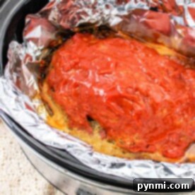 The crockpot meatloaf recipe features a savory meatloaf covered in rich tomato sauce, slowly cooking to perfection in a foil-lined slow cooker.