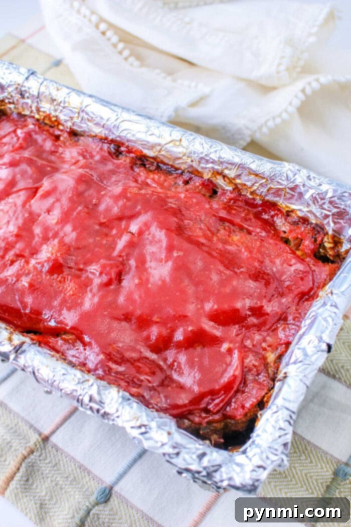 Effortless Stuffing Meatloaf 6 Stove Top Stuffing Meatloaf covered in glaze rests in a foil-lined pan on a plaid cloth, ready to be served.