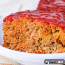 Effortless Stuffing Meatloaf 8 Close-up of a slice of Stove Top Stuffing Meatloaf topped with a tomato glaze on a white plate, ready for a comforting meal.
