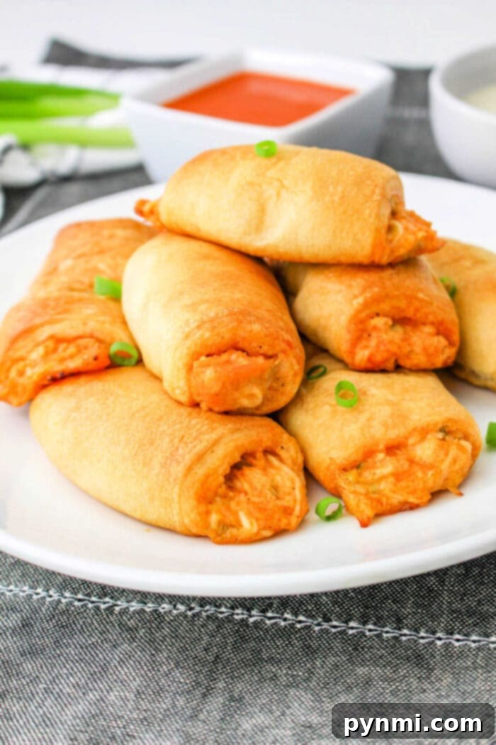 A vibrant plate filled with golden-brown Buffalo Chicken Crescent Rolls, garnished with fresh green onions and served with a side of ranch dressing for dipping. Perfect for any gathering.