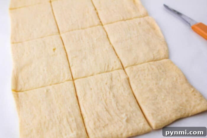 Unrolled crescent dough sheet, precisely cut into neat rectangular pieces on a white cutting board, with a chef's knife nearby, ready for filling.