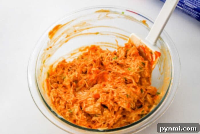 A close-up shot of a baked Buffalo Chicken appetizer, golden and flaky, revealing the savory filling within, ready to be picked up.