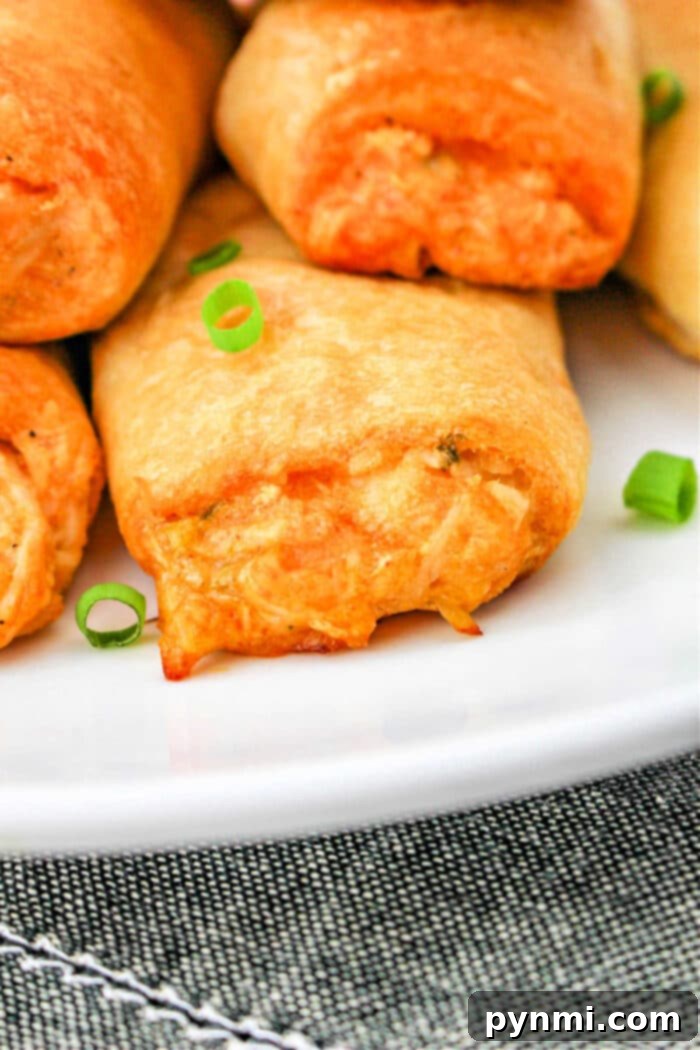 A vibrant platter of freshly baked Buffalo Chicken Rolls, generously garnished with finely chopped fresh green onions, presenting an inviting and colorful appetizer spread.