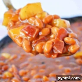 Close-up of a spoonful of apple pie baked beans with diced yellow peppers and tomatoes in a thick sauce.