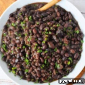 A bowl of black turtle beans cooked to perfection, garnished with chopped herbs, and elegantly served with a wooden spoon. Discover how to cook these delightful beans and elevate your culinary experience.
