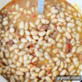 A pot of Peruvian beans simmered with tomatoes and pieces of meat in a flavorful broth.