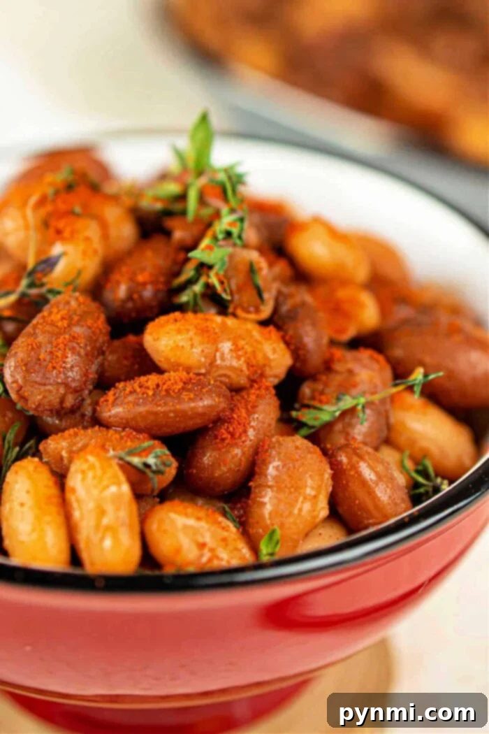 Close-up of seasoned baked tepary beans in a red bowl, garnished with sprigs of thyme.