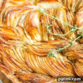 Golden-brown potato tart galette garnished with fresh thyme on a wooden board.
