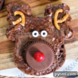 Yuletide Chocolate Squares 7 Reindeer-shaped Christmas brownies adorned with pretzel antlers, candy eyes, and a red nose rest on a wooden surface.