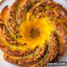 A beautifully swirled Pecan Bundt Cake, generously topped with chopped nuts and elegantly drizzled with glaze, presented on a pristine round plate.