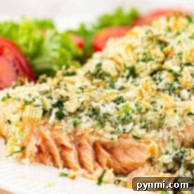 Close-up of herb-crusted salmon fillet with a crispy finish on a white plate, garnished with lettuce and tomato slices.
