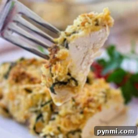 A fork holds a piece of herbed crusted chicken over a plate with garnished chicken.