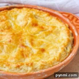 Golden-brown pie with a delectable sourdough pie crust in a round, orange baking dish on a light surface, accented by a checkered cloth in the background.