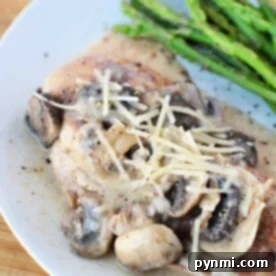 Creamy Chicken Mushroom Delight 11 Creamy mushroom chicken, infused with Chicken and Cream of Mushroom Soup, topped with cheese, served alongside asparagus on a white plate.