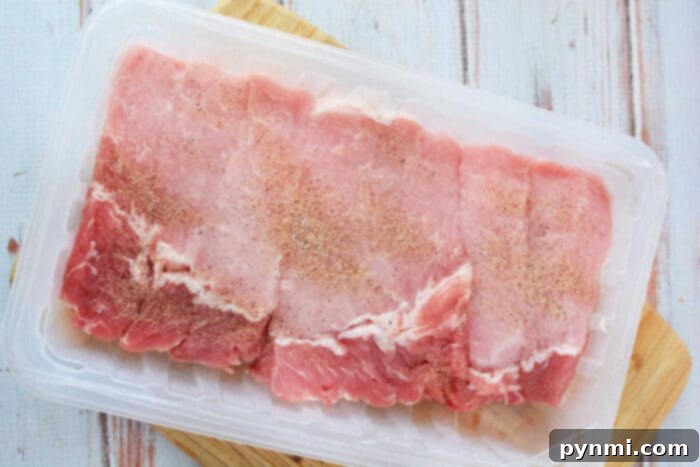 Homestyle Slow Cooker Country Ribs 3 Raw boneless ribs in a plastic tray on a wooden surface, seasoned with spices like those used for slow cooker country style ribs.