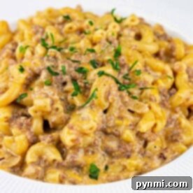 Ultimate Cheesy Beef Mac 8 A plate of creamy hamburger mac and cheese with ground beef, garnished with chopped parsley.