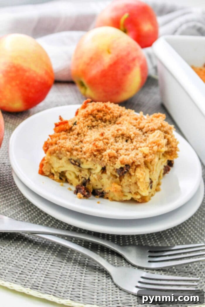 Spiced Apple Comfort Bake 8 A delectable slice of apple kugel served on a white plate with fresh apples and forks, inviting a delightful experience.