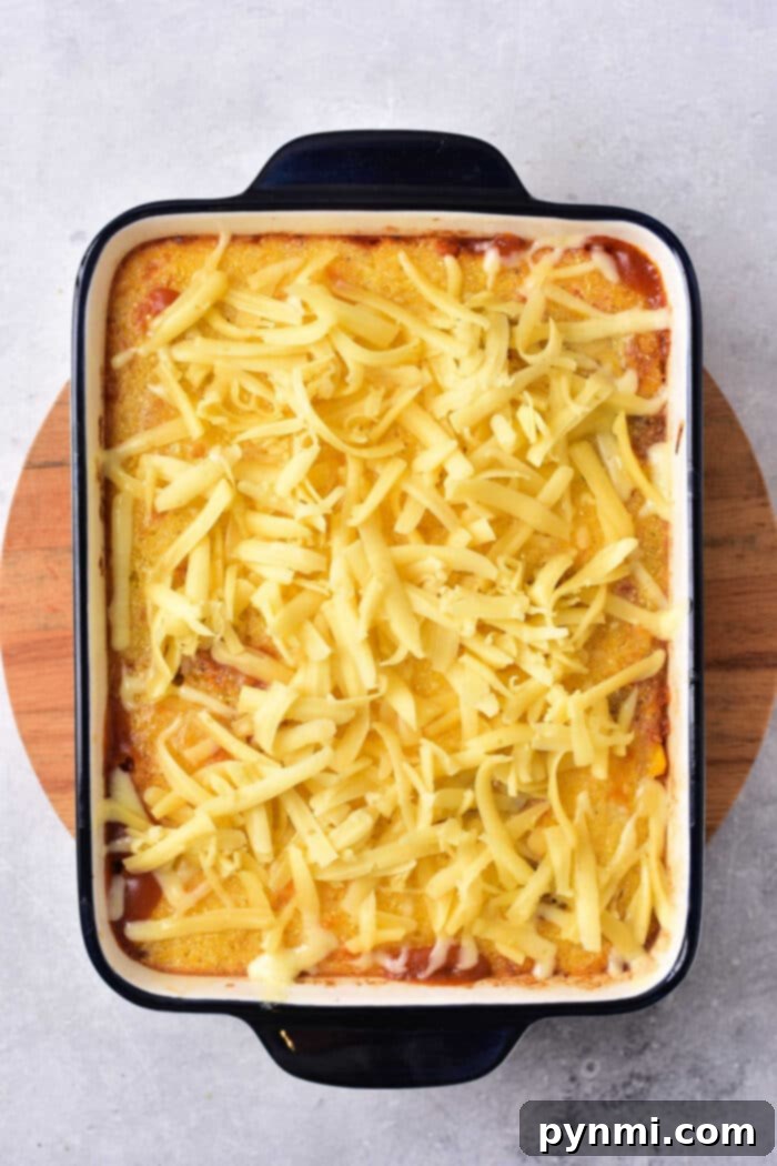 Hearty Mexican Cornbread Bake 4 A wooden board cradles a casserole dish brimming with cornbread casserole, topped with golden melted cheese, reminiscent of a comforting Mexican cornbread casserole.