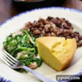 A plate featuring savory beans and cornbread alongside fresh greens, with a fork set neatly on the side.