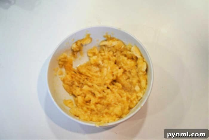 A pristine white bowl filled with perfectly mashed bananas, showing the creamy, slightly chunky texture ideal for baking. The surface is smooth, indicating proper preparation for Bananas and Cream Oatmeal, set against a clean white backdrop.