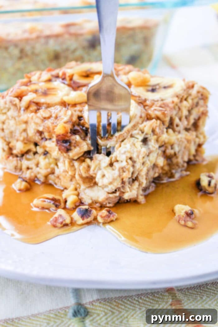 A fork elegantly plunges into a slice of creamy Bananas and Cream Oatmeal, which is perfectly baked and generously adorned with a glistening drizzle of maple syrup and a scattering of finely chopped nuts, all presented beautifully on a pristine white plate.