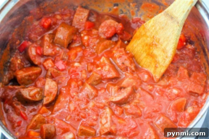 A pot of chunky tomato sauce with sausages sits invitingly, its rich aroma filling the air. Next to it, a wooden spoon rests, ready to twirl into a perfect blend reminiscent of sausage spaghetti.