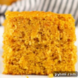 A close-up of a square piece of sweet potato cornbread on a white surface, showcasing its soft, crumbly texture.