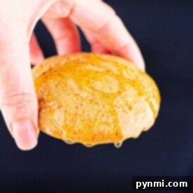 A hand holds a cornbread cookie drizzled with honey, set against a dark background.