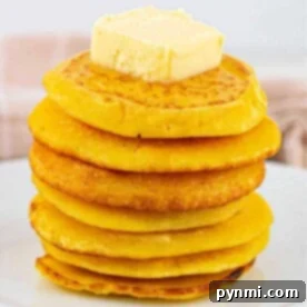 A stack of golden fried cornbread, topped with butter on a pristine white plate.