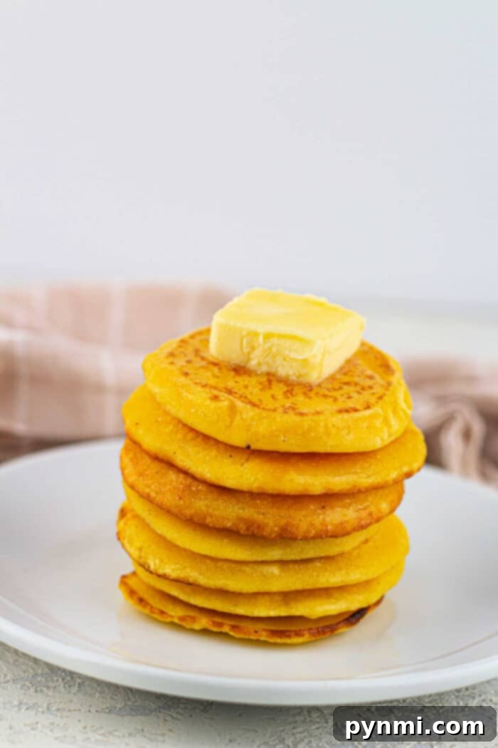 Crispy Skillet Cornbread 7 A stack of cornbread pancakes with a pat of butter on top, served on a white plate alongside golden slices of fried cornbread.