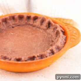 Deep Cocoa Pie Base 9 A rich chocolate pie crust sits elegantly in a ceramic dish on a beige surface, complemented by a soft cloth in the background.