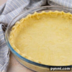 A dairy-free pie crust rests in a glass dish, perfectly prepared beside a blue and white striped cloth, ready for your favorite filling.