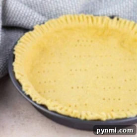 A Bisquick pie crust sits in a round black pan with crimped edges, perfectly complementing the nearby textured cloth.