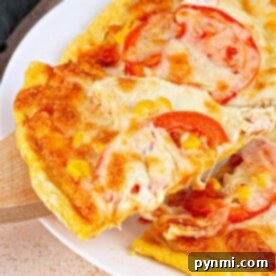 Close-up of a cheesy pizza slice with tomatoes on a cornmeal pizza crust being lifted from the whole pie on a white plate.